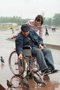 Woman and man on a wheelchair feeds birds in park